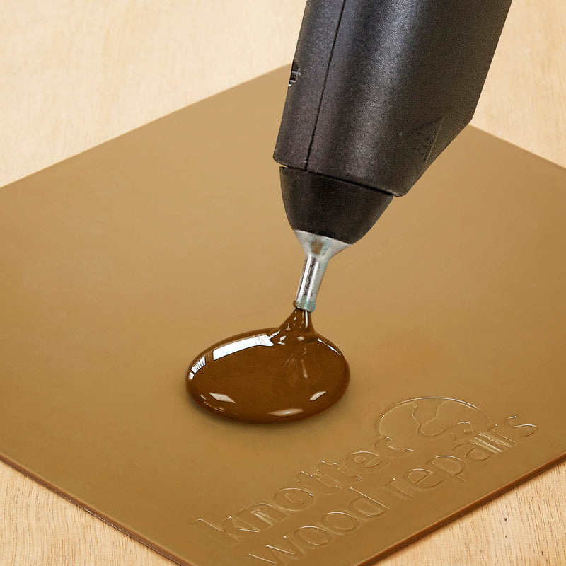 Tec 806-12 glue gun dispensing melted adhesive onto a brown non-stick silicone mat for easy handling and cleanup.